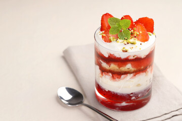 Tasty trifle dessert. Strawberries, sponge cake and whipped cream in glass on beige table, space for text