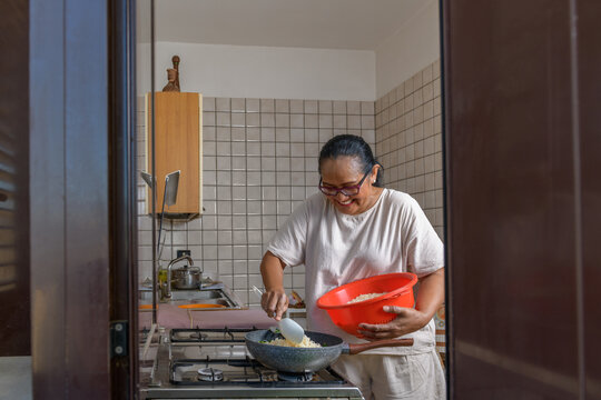 Smiling indonesian woman cooking fried rice, window framing
