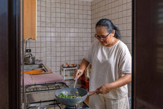 Indonesian woman cooking fried rice in the kitchen, window framing