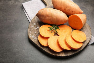 Fresh raw sweet potatoes, rosemary and salt on gray table, space for text