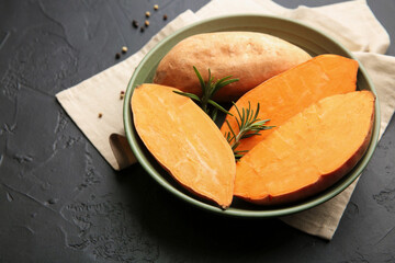 Fresh raw sweet potatoes and rosemary in bowl on dark gray textured table, closeup