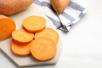 Fresh sweet potatoes and kitchen towel on white table, closeup. Space for text