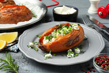 Tasty cooked sweet potatoes served with feta cheese on grey wooden table, closeup