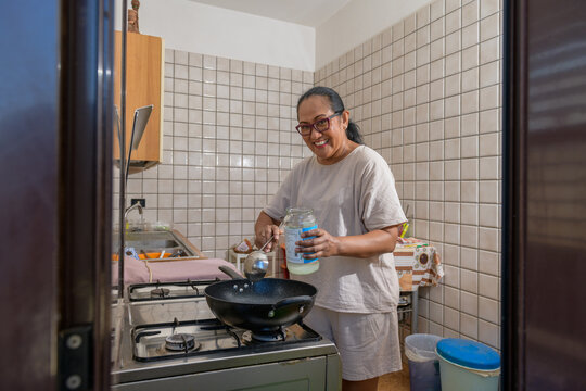 Happy indonesian woman pours coconut oil into a pan