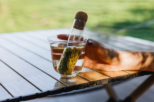 Hand holding a glass of tea with infuser on a wooden table