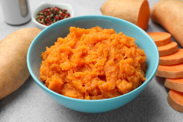 Tasty mashed sweet potato in bowl and fresh vegetables on gray table, closeup