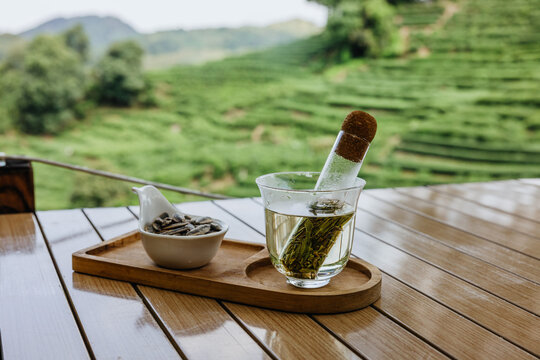 A c of green tea and sunflower seeds on a table overlooking tea fields