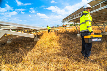 A technician in high visibility safety gear inspects the underside of a solar panel at a solar...