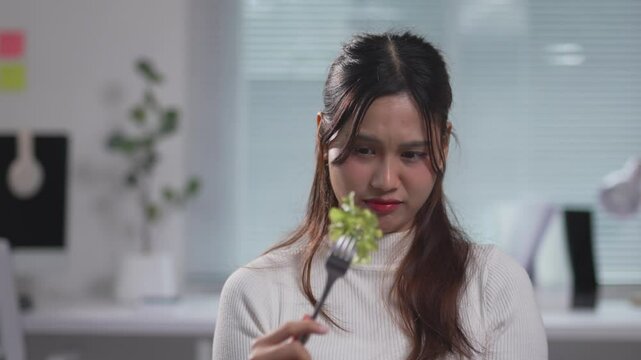 Young female experiencing visible disgust while consuming leafy greens, struggling with unappealing healthy meal in home kitchen setting