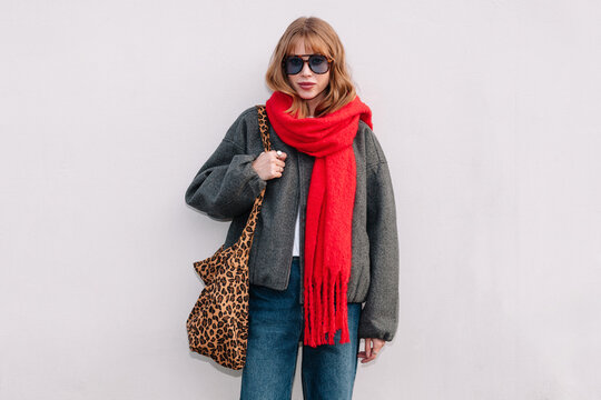 Woman wearing oversized jacket and red scarf stands against the wall