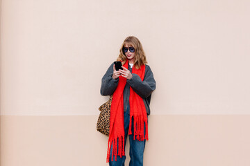 Young woman in sunglasses and a red scarf using smartphone on street