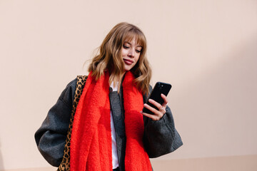 A young woman checks her smartphone while wearing autumn outfit