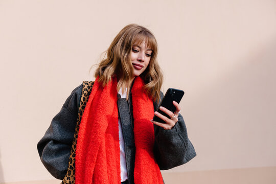 A young woman checks her smartphone while wearing autumn outfit