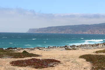 Rocky coastline at Guincho Beach, Cascais, Portugal, with the Atlantic Ocean and cliffs in the distance.