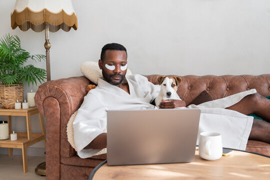 Relaxed Man Holding Dog While Using Laptop At Home