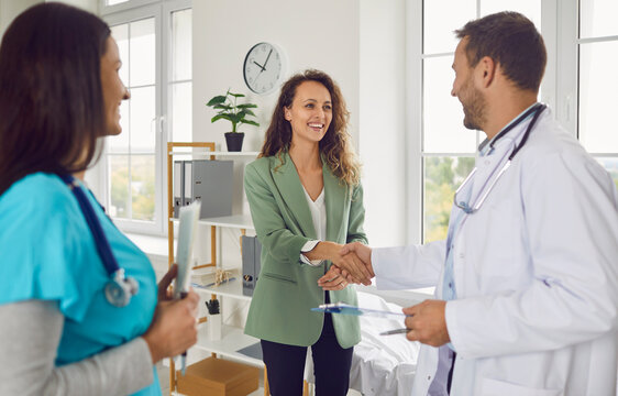 Male doctor shaking hands with a happy female patient during a medical consultation in the hospital office. The nurse and medical team provide care and support in the clinic setting.