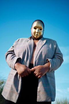A figure in a gold mask poses under the blue sky