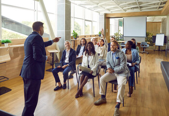 Smiling young woman raising hand to ask or answer a question on a business meeting. Group of...