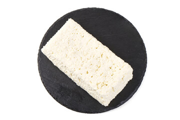 Fresh block of cottage cheese on a black slate plate, isolated on white background.