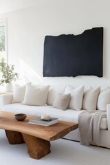 A black framed painting hangs on the wall above a white couch. The couch is covered in white pillows and a brown blanket. A wooden coffee table sits in front of the couch