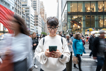 Smiling woman using smartphone on busy manhattan street, new york city