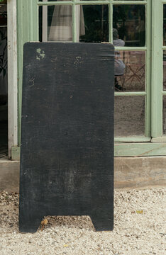 A weathered blackboard stands outside a charming caf&eacute; in daylight