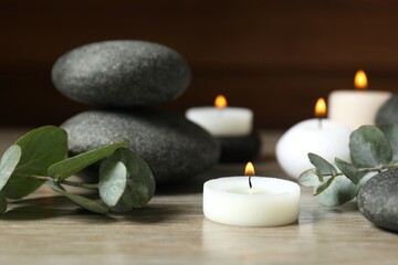 Beautiful composition with burning wax candles, stones and eucalyptus on the tablе