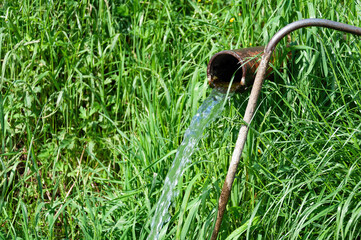 Clear Water Flowing from a Metal Pipe Against Green Grass