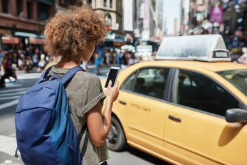 Busy summer morning in the city with a woman looking at her smartphone while waiting for a taxi