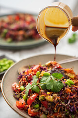 Action shot of dressing being added to quinoa bowl with tomatoes, cherry, carrot and soy sauce dressing.