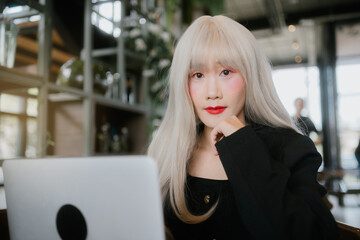 woman with long blonde hair and red lipstick sits at laptop, deep in thought