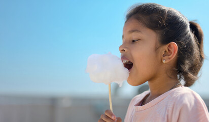 Girl enjoying sweet cotton candy treat on a sunny day.  Happy child outdoors.