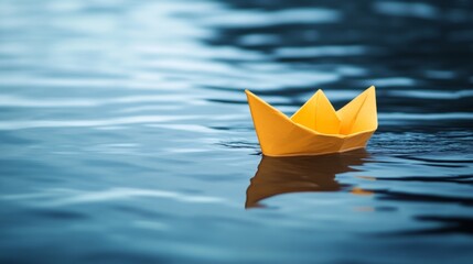 Small yellow paper boat floats on calm blue water.