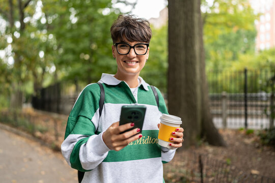 Smiling student using smartphone and drinking coffee in manhattan park