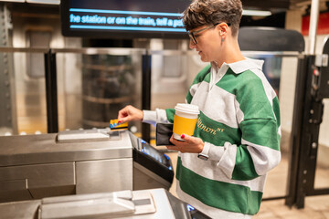 Woman using credit card and holding coffee at subway turnstile