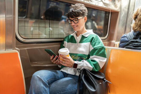 Woman using smartphone and drinking coffee on new york city subway
