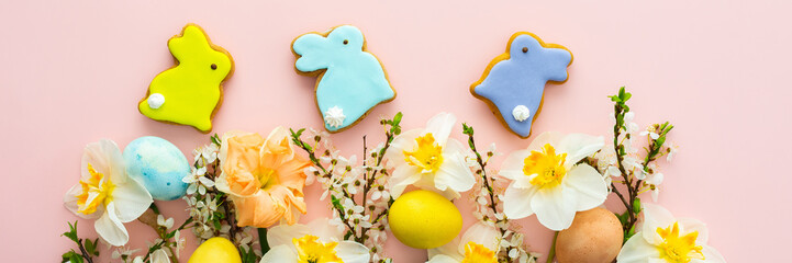 Festive banner with spring flowers and naturally colored eggs and Easter bunnies, white daffodils and cherry blossom branches on a pink pastel background