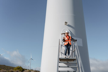 Female engineer inspecting wind turbine with digital tablet on a windy day