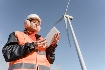 Naklejka premium Female engineer inspecting wind turbine with digital tablet in cold weather