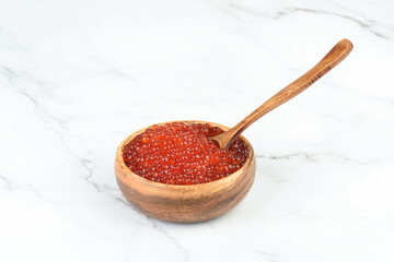 Wooden spoon in red salmon caviar inside a wooden bowl.
