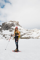A cheerful adventurer with trekking poles poses against the magnificent snowy peaks of the Picos de Europa, embodying the joy of outdoor winter activities in the mountains.