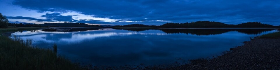 Fototapeta premium Serene twilight over a calm lake reflecting the sky and surrounding landscape.