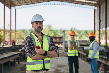 A man in a yellow vest stands in front of a building with two other men in orang
