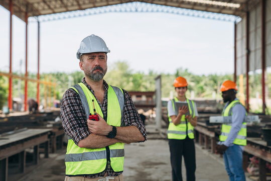 A man in a yellow vest stands in front of a building with two other men in orang - Powered by Adobe