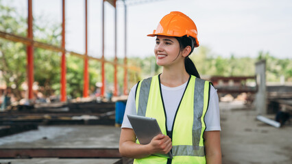 A woman wearing a safety vest and a hard hat is holding a tablet