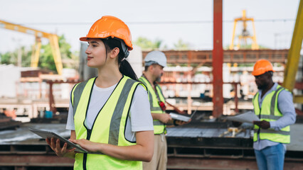 A woman wearing a yellow vest and an orange hard hat is holding a tablet