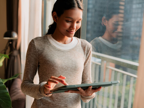 Young Woman Using Digital Tablet by Window at Home