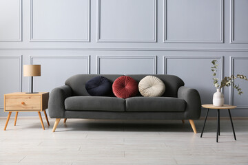 Stylish sofa with cushions, lamp and eucalyptus branches in vase on side tables in room
