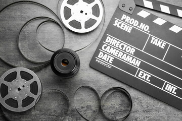 Flat lay composition with movie clapper, film reels and camera lens on grey textured table