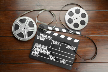 Movie clapper and film reels on wooden table, flat lay